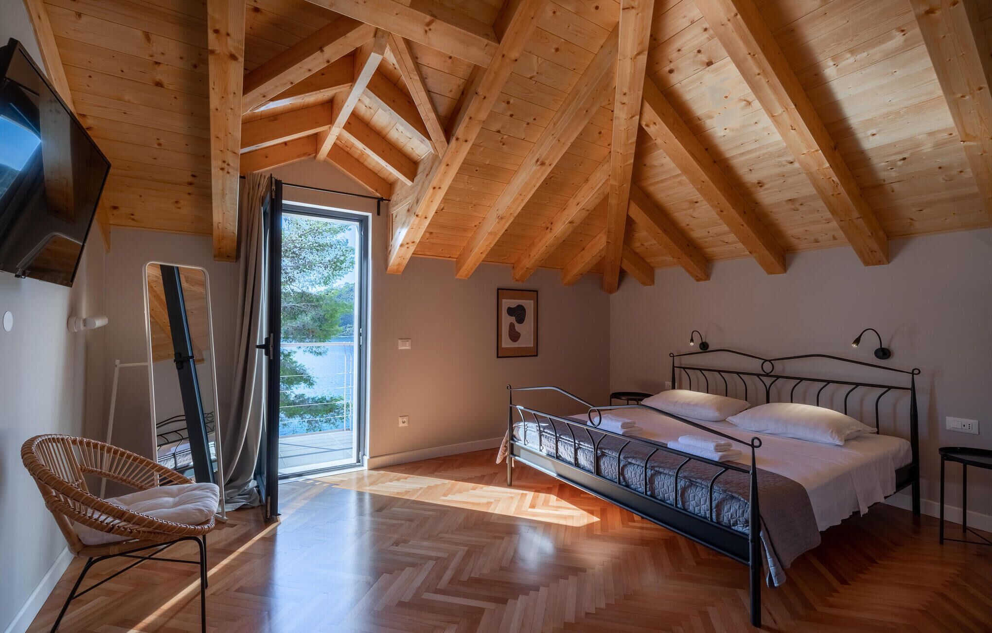 Ein Schlafzimmer mit Holzboden, einem Bett mit Metallgestell, einem Sessel und einer Tür, die auf einen Balkon führt.