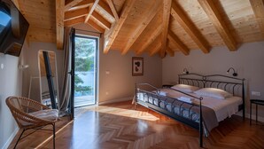 Ein Schlafzimmer mit Holzboden, einem Bett mit Metallgestell, einem Sessel und einer Tür, die auf einen Balkon führt.