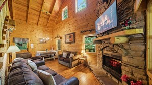 A log cabin interior with a fireplace, wooden walls, a sofa, and a television. - Log Cabin, UTK/Neyland, Smokies, 16acres, FP, HotTub, GameRoom, Fishing, Pets (Knoxville)