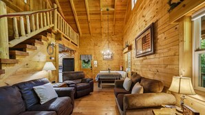A log cabin interior with a staircase, leather sofas, a dining table, and a chandelier. - Log Cabin, UTK/Neyland, Smokies, 16acres, FP, HotTub, GameRoom, Fishing, Pets (Knoxville)