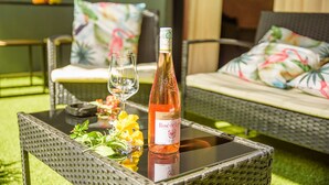 En flaska rosévin står på ett glasbord tillsammans med ett glas vatten och en gul blomma.