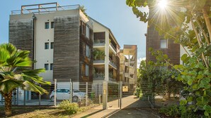 En modern bostadsbyggnad med flera våningar, balkonger, en grind vid entrén och omgivande grönska.