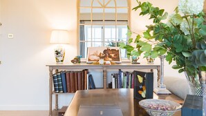 A room with a wooden table, books, a framed picture, a lamp, and a potted plant.