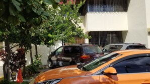 Un estacionamiento con un auto amarillo, un edificio con balcones y algo de vegetación.