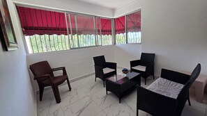 A room with a glass table, four chairs, a window with red curtains, and a view of greenery outside. - Best place to stay, close to everything, you will love it. (Santo Domingo)