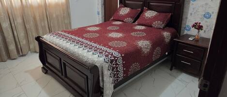 A bedroom with a wooden bed, a bedside table, a nightstand, and a wall with floral wallpaper.