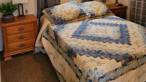 Une chambre à coucher comprenant un lit, deux tables de chevet, un ventilateur de plafond, une fenêtre avec des rideaux et des éléments de décoration murale.