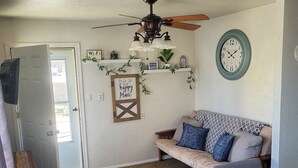 Un salon chaleureux avec un canapé, une table à manger et un ventilateur de plafond. Il y a une horloge au mur et une pancarte sur laquelle on peut lire : « Ici, nous sommes heureux. »