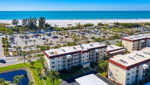 A multi-story hotel with a parking lot, surrounded by palm trees and a beach in the background. - Siesta Key Beach Condo #1 Beach (Siesta Key)