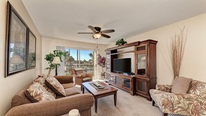 A living room with a sofa, armchair, coffee table, TV, and a ceiling fan. - Siesta Key Beach Condo #1 Beach (Siesta Key)