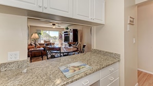A kitchen with white cabinets, a granite countertop, and a dining area with a table and chairs. - Siesta Key Beach Condo #1 Beach (Siesta Key)