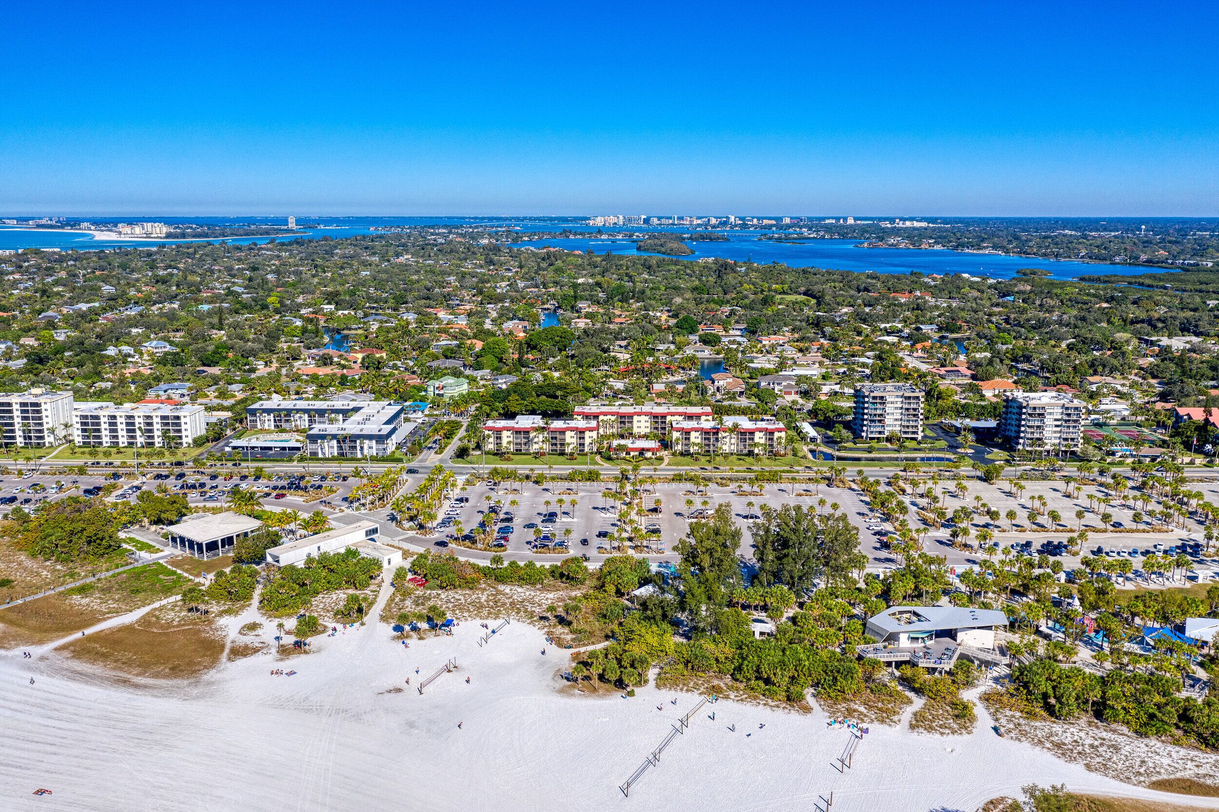An aerial view of a coastal area with a large hotel complex, parking lots, and a beach.
