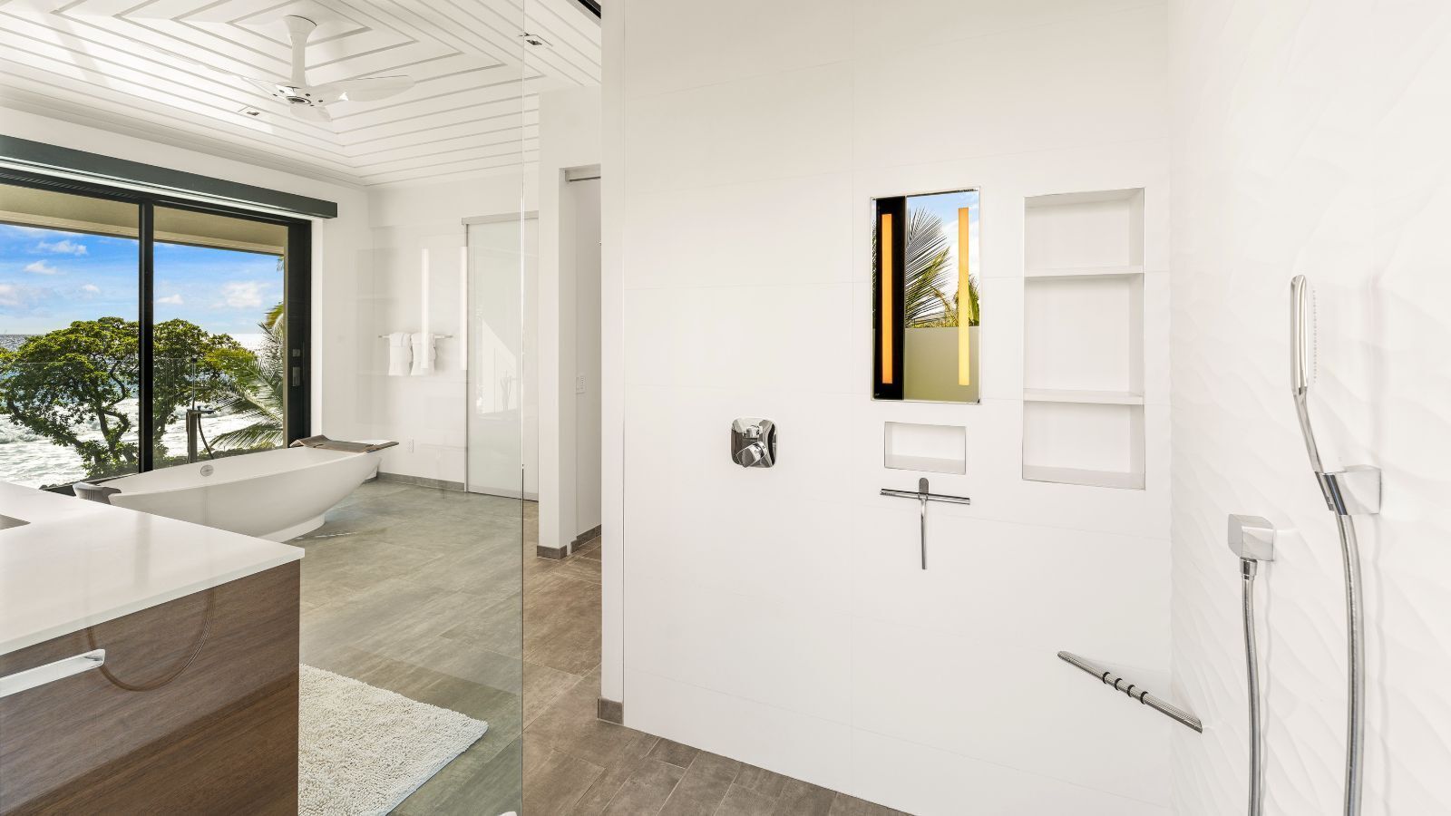 Een moderne badkamer met een bad, een douche en een groot raam met uitzicht op de natuur.
