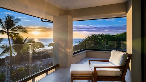 A balcony with a view of the ocean and palm trees at sunset. - "Iron Man Available" Private Oceanfront Villa W/ detached Ohana and Private Pool (Kailua-Kona)