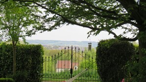 Un jardín con una hamaca roja, una reja de metal y vistas a una casa y un paisaje lejano.