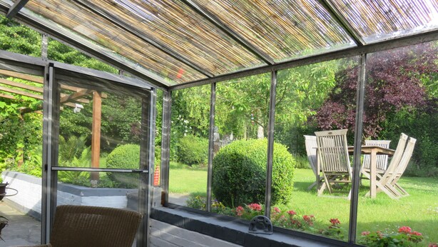 Un invernadero con techo de cristal, mobiliario de mimbre y vistas a un jardín cuidado.