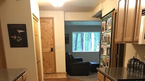 A kitchen with wooden cabinets, a stainless steel oven, and a refrigerator. There is a window with a view of trees and a door leading to a living area. - Two bedroom, fully furnished apartment with private entrance on 3 wooded acres (Fairbanks)