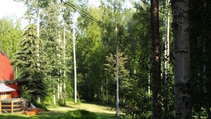 A forested area with a red building, likely a cabin or lodge, surrounded by tall trees and a clear sky. - Two bedroom, fully furnished apartment with private entrance on 3 wooded acres (Fairbanks)