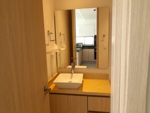 Un baño con tocador de madera, lavamanos blanco y espejo.