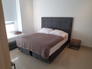 Un dormitorio moderno con una cama grande, una mesita de noche pequeña y una ventana con persianas.