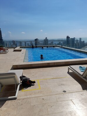 Una piscina en la azotea con agua cristalina, rodeada de sillones de descanso y vistas a la ciudad.