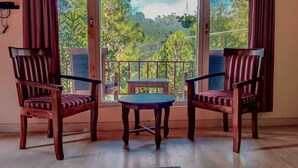 A room with two wooden chairs and a small table, a window with a view of greenery, and a curtain on the left. - Majkhali Woods, Ranikhet, By Himalayan Eco Lodges (Ranikhet)