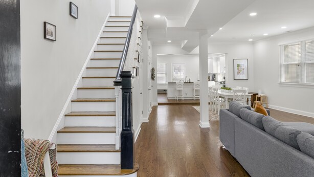 A spacious living area with a staircase, a gray sofa, and a dining area in the background. - Book with us ⭐️3 bd 2.5 ba in Historic Washington DC Home (Washington)