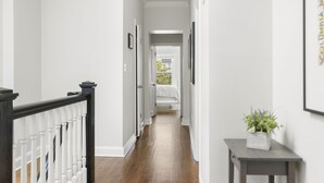 A hallway with a wooden floor, white walls, and a dark wooden railing. There is a small table with a plant on the right side. - Book with us ⭐️3 bd 2.5 ba in Historic Washington DC Home (Washington)