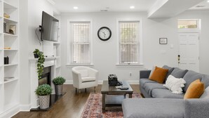 A living room with a fireplace, a grey sofa, a white armchair, and a coffee table. - Book with us ⭐️3 bd 2.5 ba in Historic Washington DC Home (Washington)