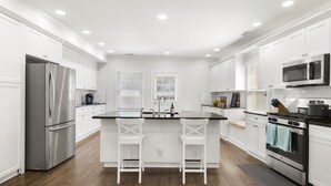 A modern kitchen with white cabinets, stainless steel appliances, and a central island with bar stools. - Book with us ⭐️3 bd 2.5 ba in Historic Washington DC Home (Washington)