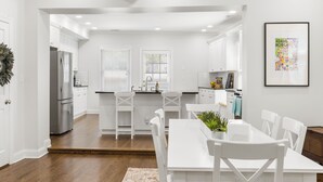 A modern kitchen with white cabinets, stainless steel appliances, and a dining area with white chairs and a table. - Book with us ⭐️3 bd 2.5 ba in Historic Washington DC Home (Washington)