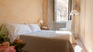 A bedroom with a bed, a nightstand, a chair, and a window with a view of buildings.