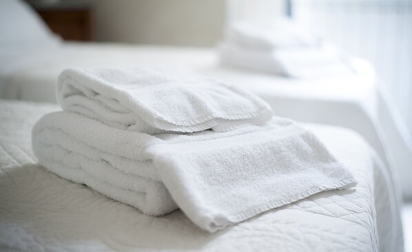 A neatly folded stack of white towels on a bed with a quilted cover.