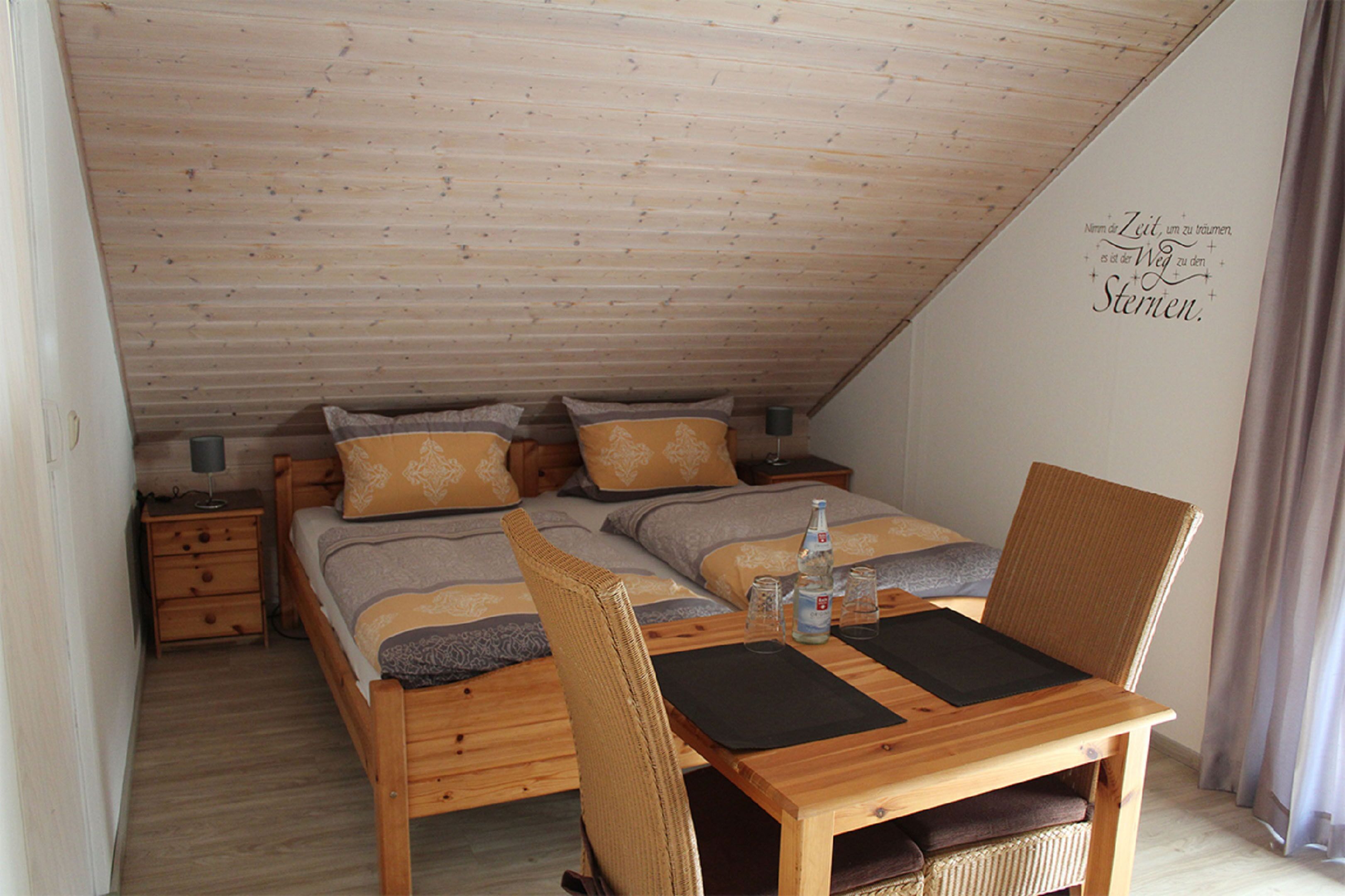 A bedroom with two beds, a wooden table, and a chair.