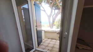 Eine offene Schiebetür führt zu einem Balkon mit Fliesenboden und Blick auf Bäume sowie ein Gewässer.