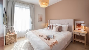 A modern bedroom with a large bed, bedside tables, a hanging light fixture, and a window with curtains. - Nasma Luxury Stays- Murjan 6, Jumeirah Beach Residence (Dubai)