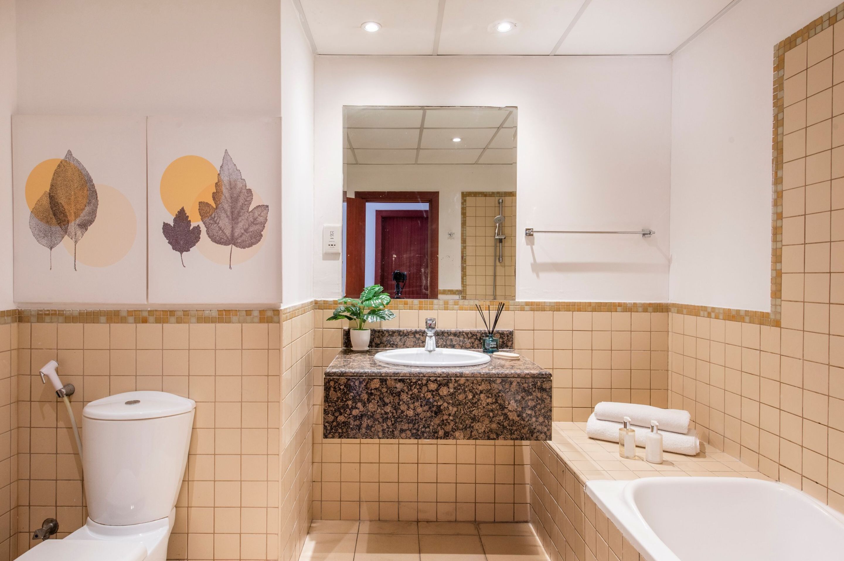 A bathroom with a toilet, sink, and bathtub. There are decorative leaf patterns on the wall and a mirror above the sink.