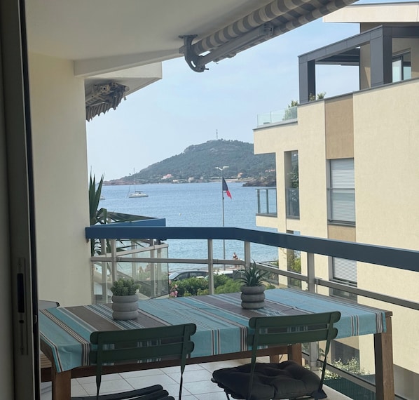 A balcony with a view of the sea, a flag, and a table with chairs.