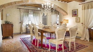A dining room with a wooden table, white chairs, a chandelier, and a red patterned rug.