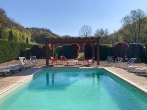 Ein rechteckiger Pool mit einer Holzpergola und roten Stühlen im Hintergrund.