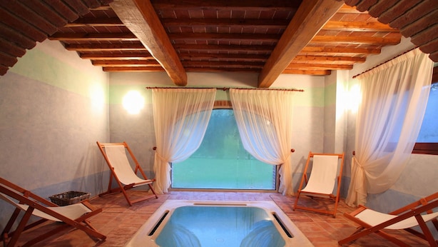 A spa room with a hot tub, wooden beams, and two wooden chairs.