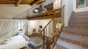 A bedroom with a bed, a window with curtains, a staircase, and a chair.
