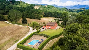 An aerial view of a property with a swimming pool, a red building, and surrounding greenery.