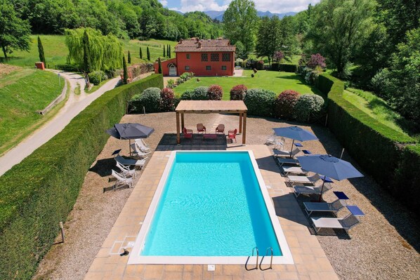 Ein rechteckiger Pool mit einer Pergola und Liegestühlen.