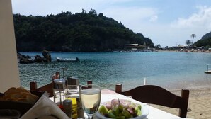 Ein Tisch mit verschiedenen Speisen, einem Glas Weißwein und Blick auf Strand und Wasser.