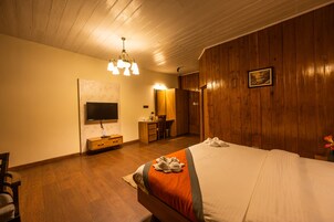 Habitación de hotel con techo de madera, una cama con manta naranja, un escritorio con silla, televisor y un armario de madera.