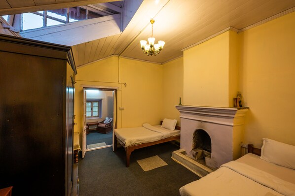 A room with two beds, a fireplace, a chandelier, and a door leading to another room. - Arcadia Heritage Resort (Darjeeling)