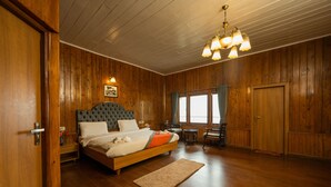 A wooden-paneled bedroom with a large bed, a chandelier, and a view of the outdoors through a window.