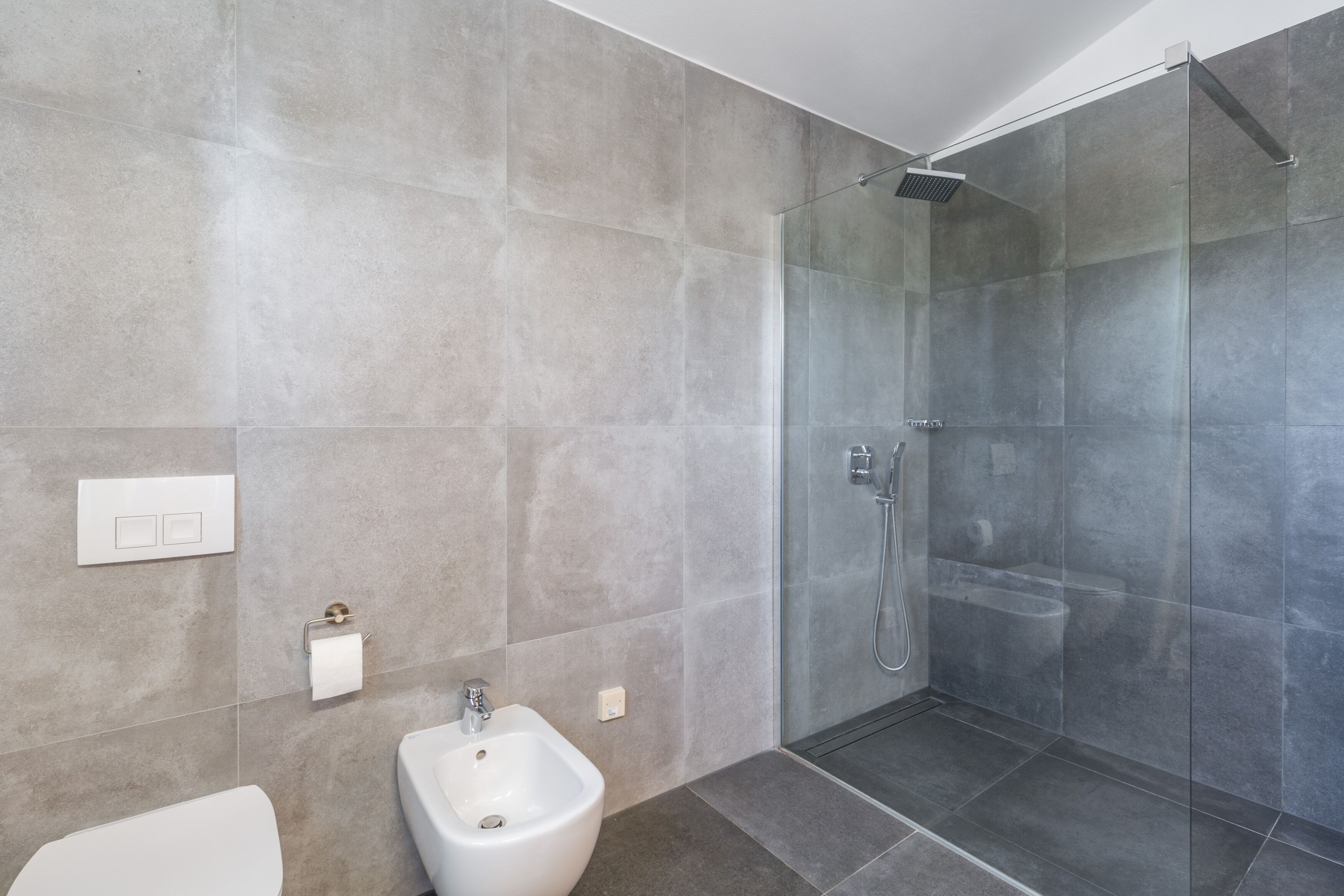 A modern bathroom with a glass-enclosed shower, a bidet, and a toilet.