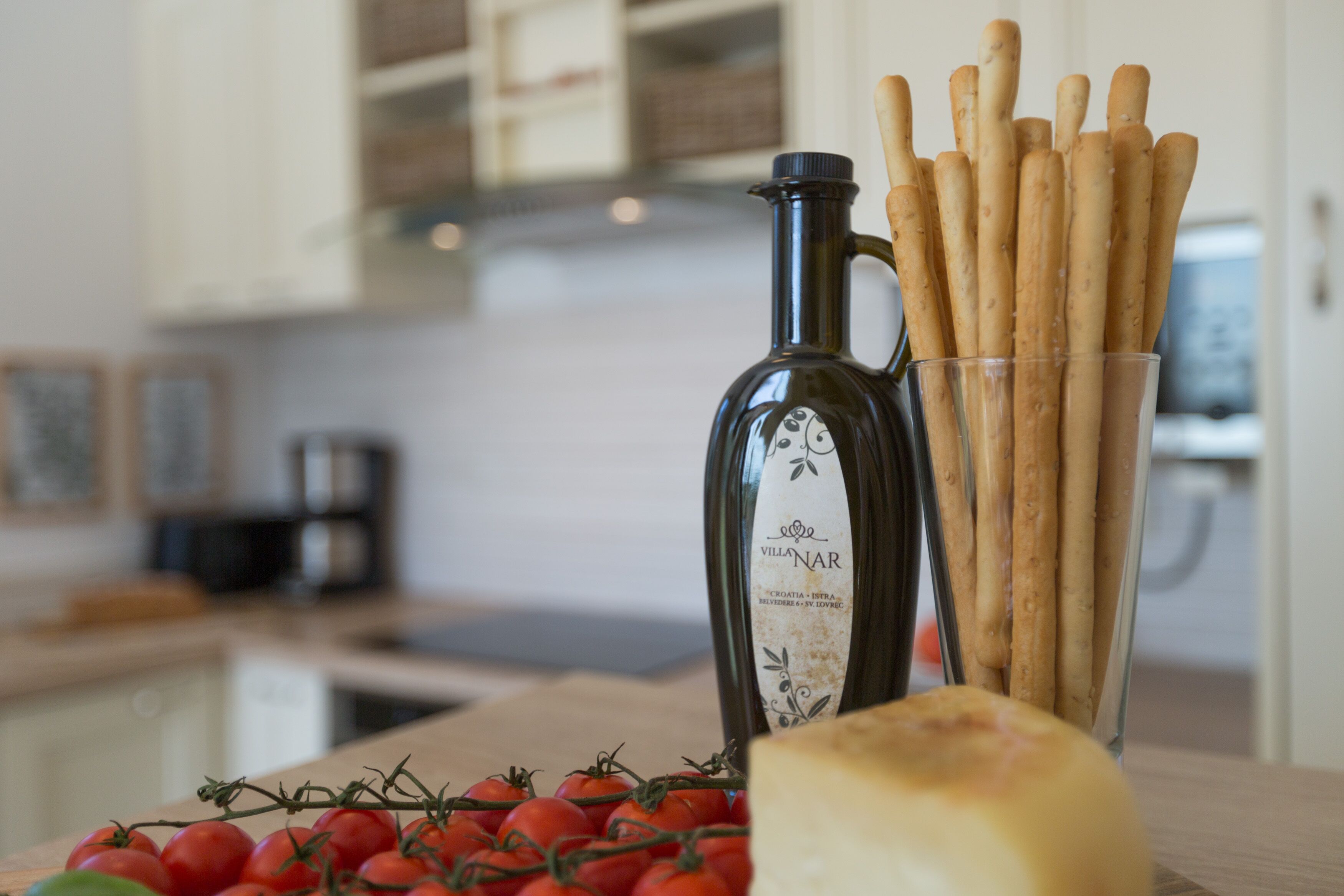 A kitchen counter with a bottle of Villanar wine, a glass of breadsticks, and a bunch of tomatoes.